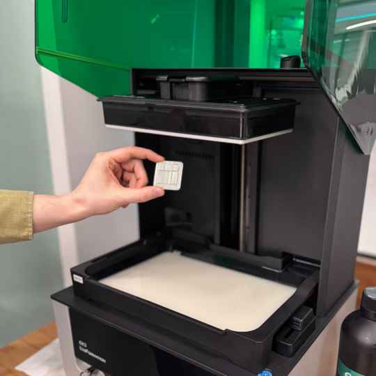 Im Bild ist ein geöffneter SLA-Drucker mit grünem Verdeck un