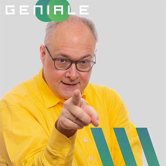 Person mit Brille in gelbem Hemd zeigt direkt auf Betrachter